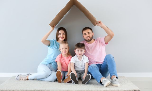Familie unter einem Hausdach aus Karton